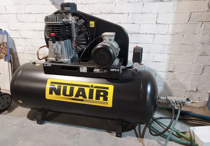 Un compresor de uña NUAIR, negro, con etiqueta amarilla y detalles plateados. Ideal para tu taller.