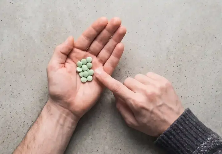 Mano aperta con un mucchietto di pillole verdi, come un trittico gocce. Un dito le indica.