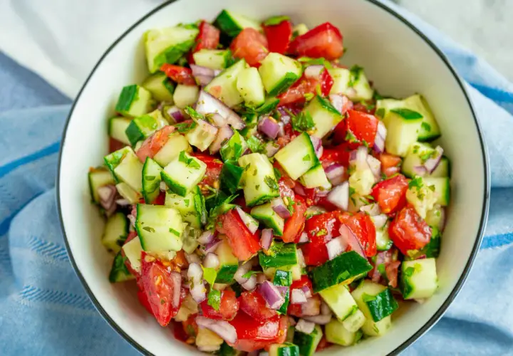 Frischer Tomaten-Gurken-Salat mit roten Zwiebeln und Kräutern, serviert in einer Schüssel.
