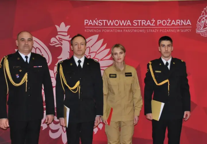 Czterech funkcjonariuszy Państwowej Straży Pożarnej w galowych mundurach i kombinezonie, z odznaczeniami i dokumentami.