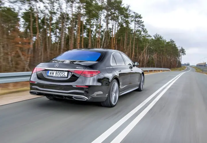 Czarny Mercedes S400d 4Matic sunie po drodze wśród drzew.