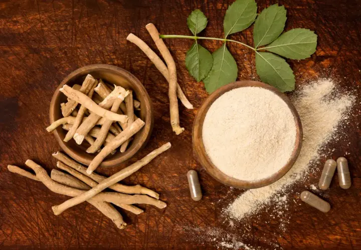 Ashwagandha roots, powder, and capsules on a wooden surface with leaves.