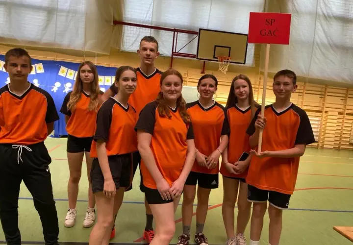 Uczniowie zespołu szkolno przedszkolnego SP GAC w pomarańczowych strojach sportowych pozują do zdjęcia w sali gimnastycznej.