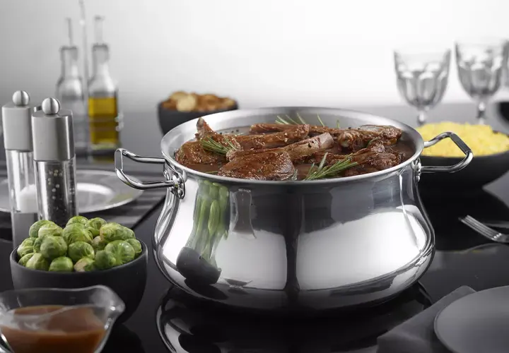 Un plat mijoté dans une cocotte en aluminium brillant, prêt pour le nettoyage. Des accompagnements comme des choux de Bruxelles et du riz sont disposés autour.