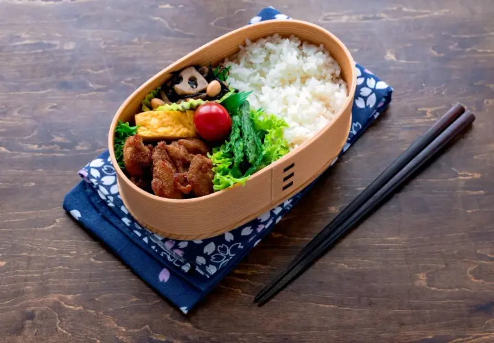 A bento box filled with rice, fried chicken, tamagoyaki, asparagus, and a cherry tomato. This is what comes in a bento box for a delicious meal.