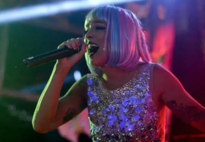 Lorena Castell, con peluca rosa y azul, canta en un escenario con un vestido brillante.