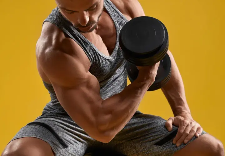 Mężczyzna ćwiczy biceps z hantlem. Widać lekkie drżenie mięśni po treningu, oznakę wysiłku.