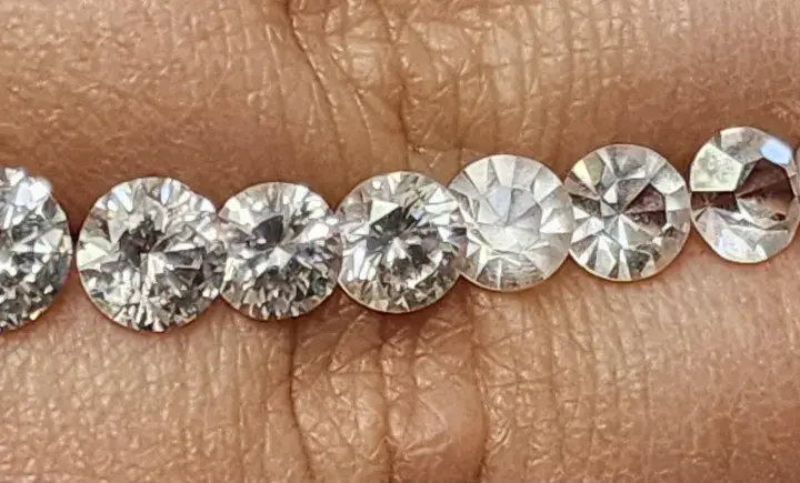 Reihe von geschliffenen Steinen, die auf einer Hautoberfläche liegen. Es ist schwierig, diamant oder zirkonia erkennen, da sie sehr ähnlich aussehen.
