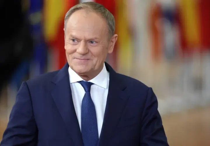 Uśmiechnięty Donald Tusk w granatowym garniturze i białej koszuli z niebieskim krawatem. Dziś Tusk robi wrażenie zadowolonego.