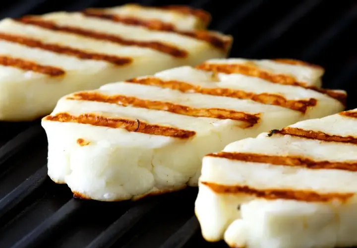 Trzy kawałki halloumi z grilla, z apetycznymi paskami, leżą na czarnej, grillowej powierzchni.