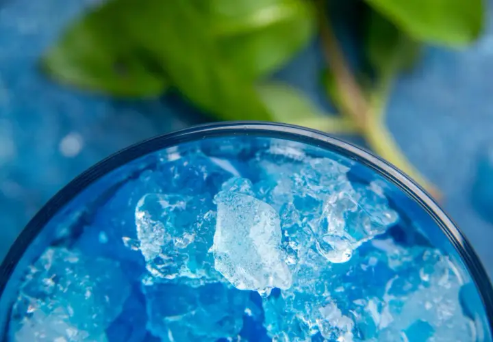Intensywnie niebieski likier Blue Curacao z kruszonym lodem w szklance, z zielonym liściem w tle.
