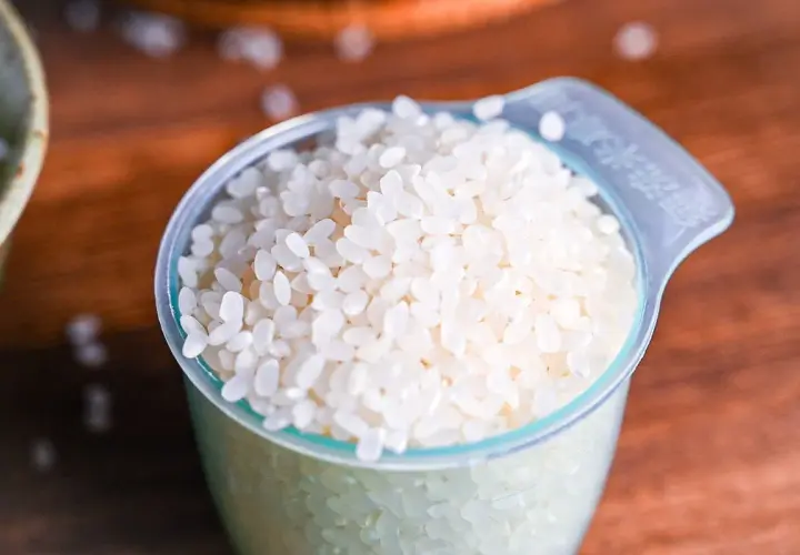 A measuring cup filled with short-grain white rice, ready for cooking Japanese rice.