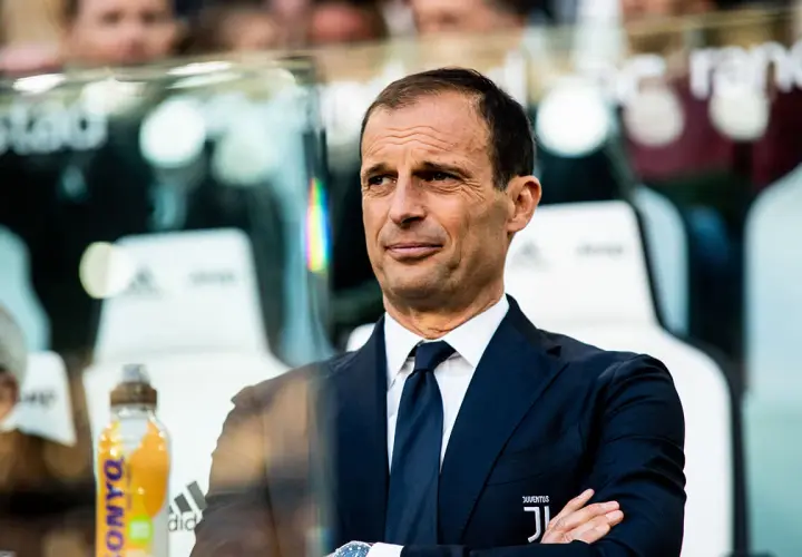 Massimiliano Allegri, w eleganckim garniturze, z rękami skrzyżowanymi na piersi, obserwuje grę.