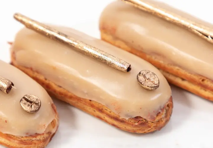 Délicieux éclairs au café, parfaits pour savoir quoi faire avec de la crème pâtissière. Ils sont décorés de grains de café dorés et d'une touche de paillettes.