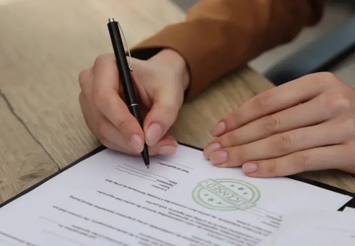 Ręka podpisuje dokument. Uważaj na zapisy, by uniknąć skutków podpisania niekorzystnej umowy wydawniczej.