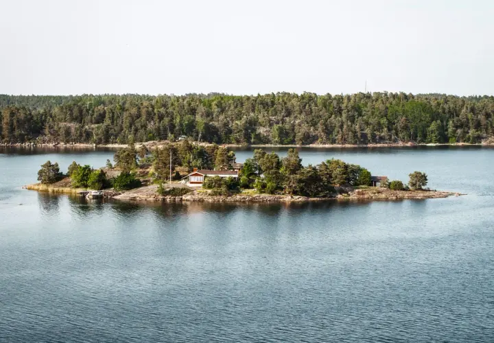 Malutka wyspa z domkiem i drzewami, część archipelagu sztokholmskiego, otoczona spokojną wodą.