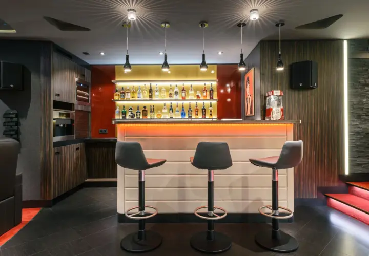 Stilvolle Bar mit beleuchteten Regalen voller Flaschen, drei Barhockern und einer Popcornmaschine. Tolle partyraum bar ideen für Ihr Zuhause.