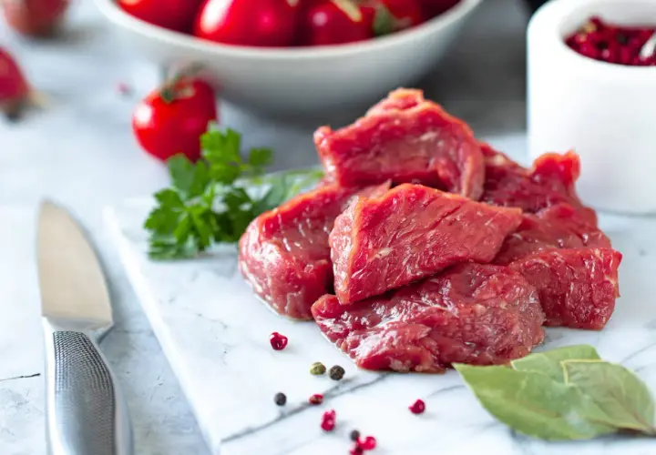 Morceaux de viande rouge crue sur une planche en marbre, avec des tomates cerises et des herbes. Question : viande hors frigo combien de temps ?