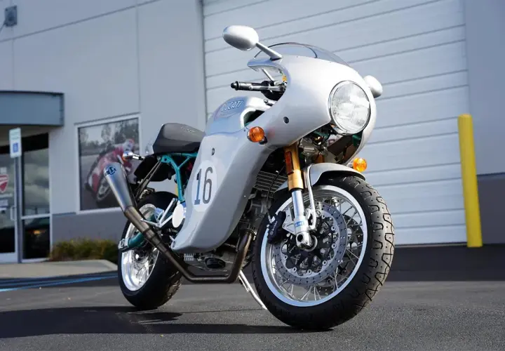Moto Ducati plateada con el número 16, inspirada en el estilo de Paul Smart, lista para la carretera.