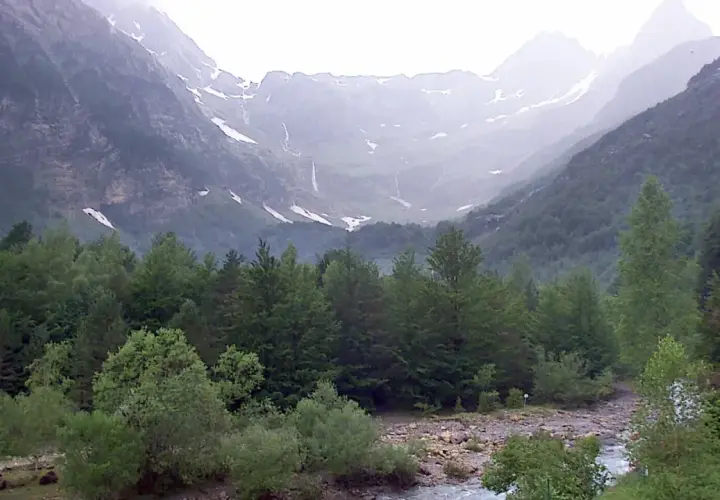 Majestuoso valle Pineta con cascadas cayendo por montañas cubiertas de nieve y un río serpenteando entre frondosos bosques verdes.