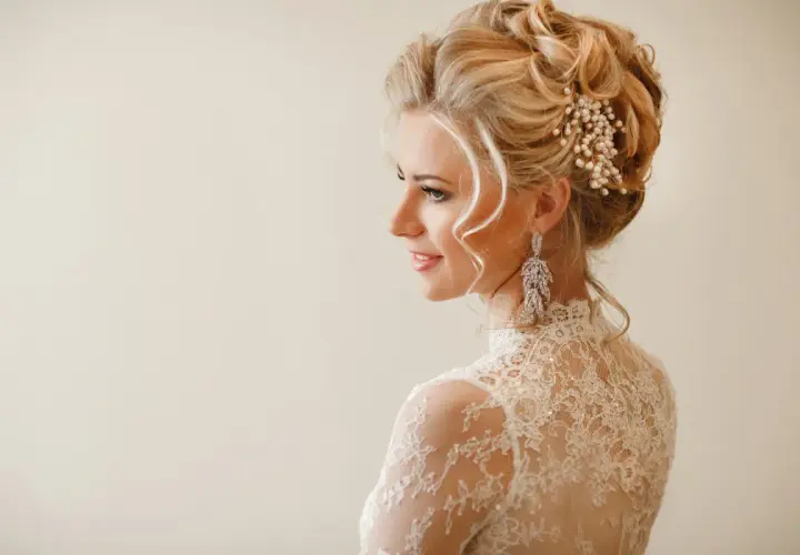 Elegancka panna młoda z upiętymi włosami ozdobionymi perłami i kryształami. Jej fryzury ślubne glamour podkreślają delikatne loki opadające na ramiona.