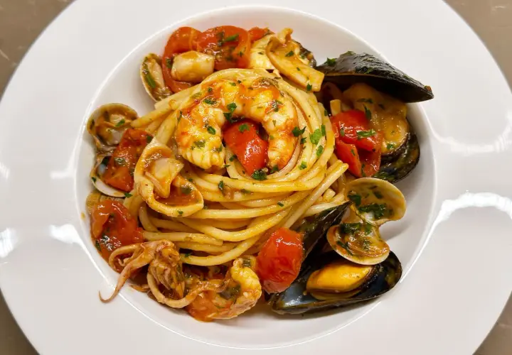 Un invitante piatto di spaghetti allo scoglio, con gamberi, cozze, vongole e calamari, condito con pomodorini e prezzemolo.