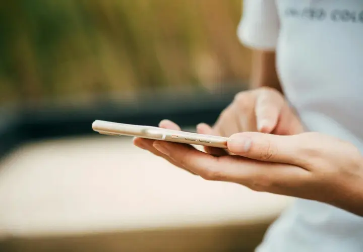 Dłonie trzymające złoty telefon. Zastanawiasz się, jak wyczyścić telefon? Oto praktyczny poradnik.