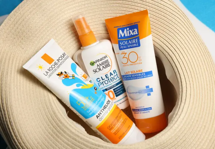 Trois tubes de crème solaire, dont une crème solaire périmée, sont posés sur un chapeau de paille.