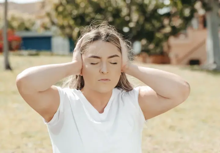 Ragazza con le orecchie tappate, occhi chiusi, espressione di ansia. Il rumore del mondo esterno è troppo forte.