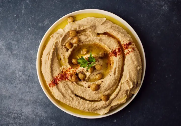 Cremoso hummus di ceci guarnito con ceci interi, paprika e prezzemolo, pronto per essere gustato.