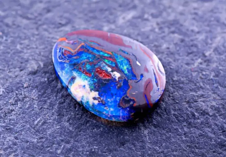 Ein faszinierender Edelstein aus Australien, ein Boulderopal, zeigt ein lebendiges Farbspiel aus Blau, Rot und Orange auf dunklem Grund.