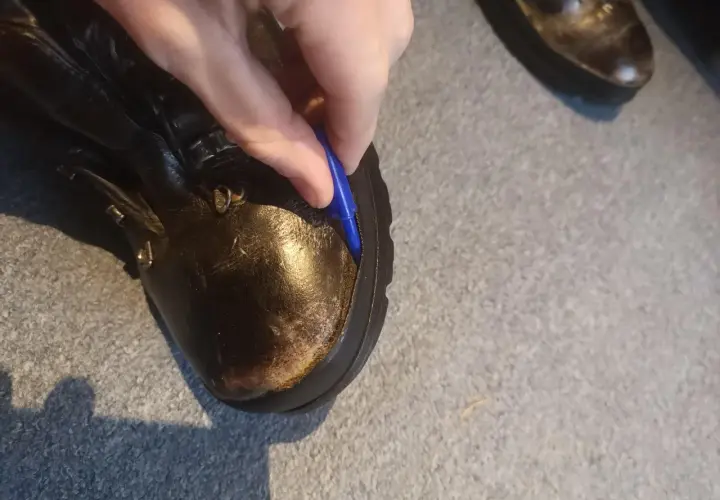 A hand uses a blue tool to pry open a seam on a leather boot, showing how to fix boots that are coming apart.