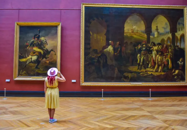 Kobieta w żółtej sukience i różowym kapeluszu podziwia obrazy w Luwrze. Co to za muzeum? To słynny paryski Luwr!