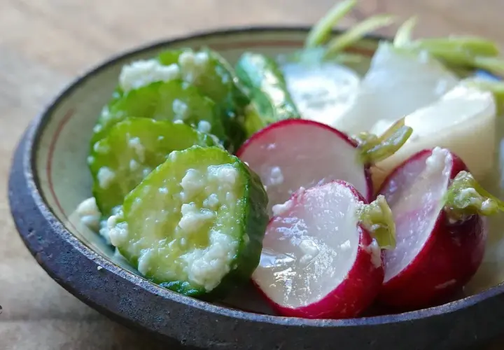 A close-up of a bowl filled with shio koji pickles. Sliced cucumbers and radishes are coated in a creamy marinade, showcasing their vibrant colors and textures.