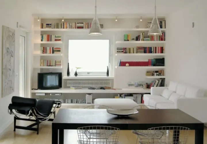 Librerie in cartongesso moderne con libri, TV, divano bianco e tavolo da pranzo.
