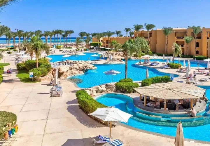 Słoneczny dzień w Stella Beach Resort & Spa Makadi Bay. Goście relaksują się przy basenach, pod palmami i parasolami.