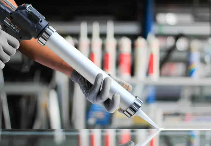 Demostración de como usar una pistola de silicona para aplicar un cordón uniforme sobre una superficie de vidrio.