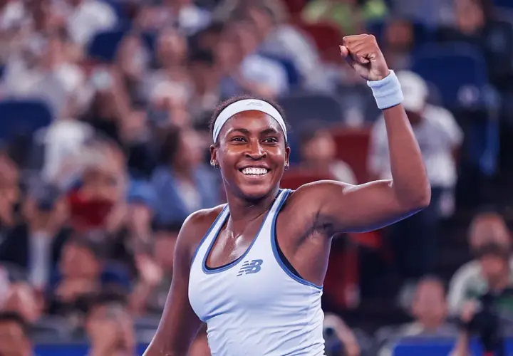Uśmiechnięta gauff tenisistka z zaciśniętą pięścią w geście triumfu, na tle rozmazanej publiczności.