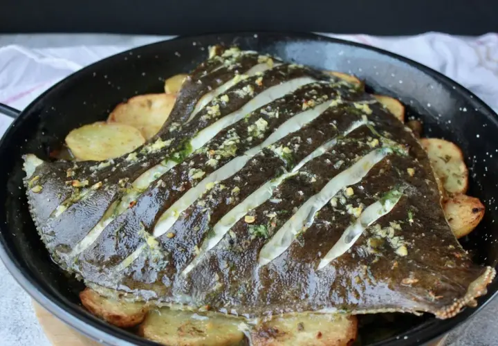 Rodaballo al horno con patatas, preparado con cortes y aderezado con hierbas y ajo.