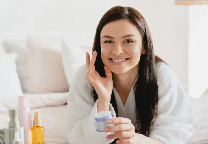 Donna sorridente applica crema viso, scoprendo i benefici di un siero probiotico per una pelle sana e luminosa.