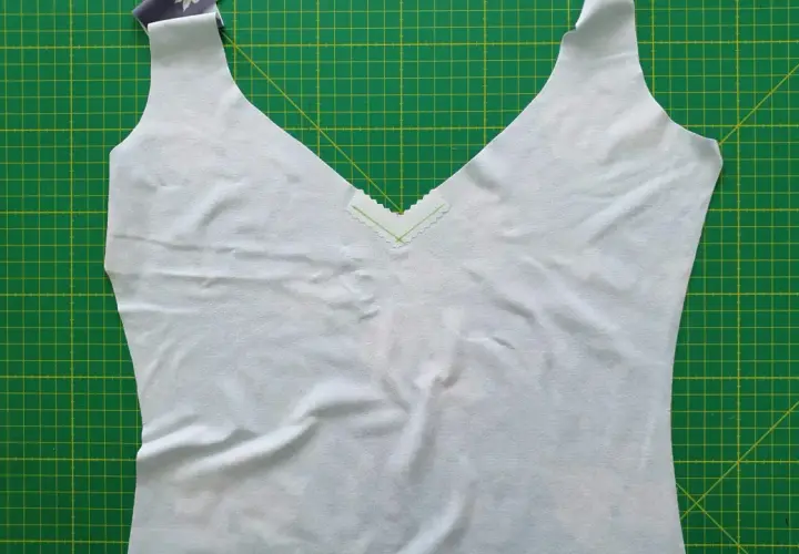 A light blue garment with a deep v neck neckline, trimmed with a delicate zigzag stitch, lies on a green cutting mat.