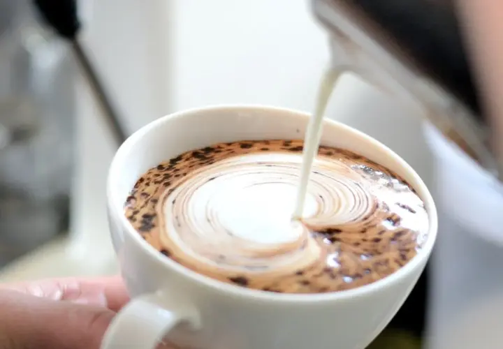 Barista wlewa mleko do kawy, tworząc wzór latte art.