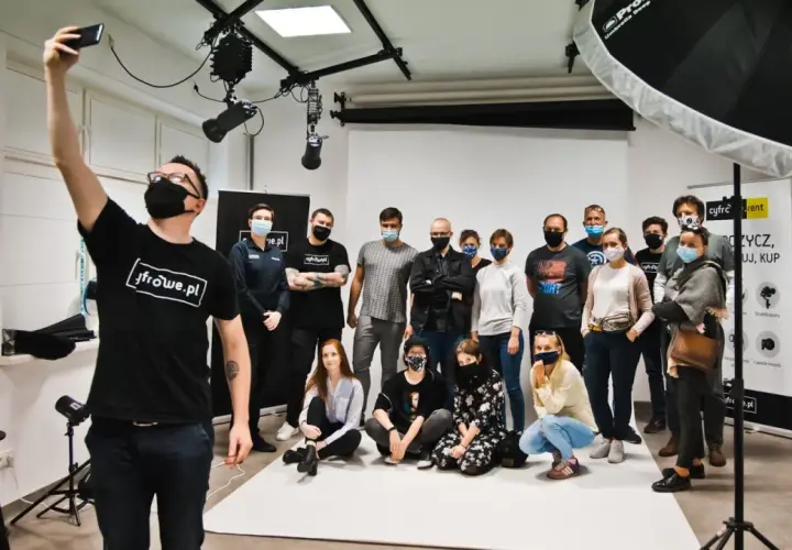 Grupa uczestników kursów foto w studiu, pozuje do wspólnego zdjęcia. Jeden z nich robi selfie.