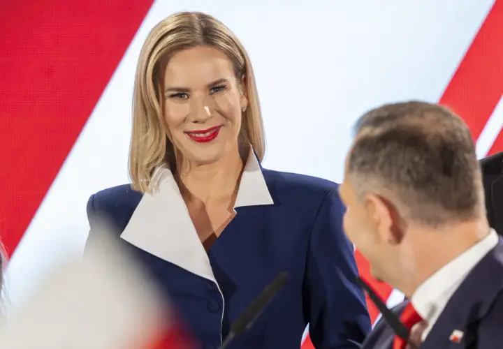 Kobieta w granatowej marynarce z białym kołnierzem uśmiecha się do mężczyzny.