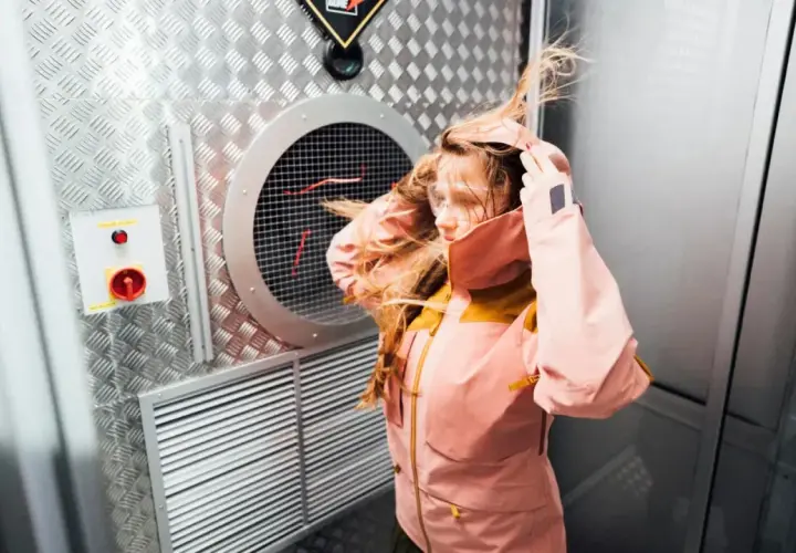 Dziewczyna w kurtce z materiału Gore-Tex co to jest, testuje jej odporność na wiatr w specjalnej komorze.