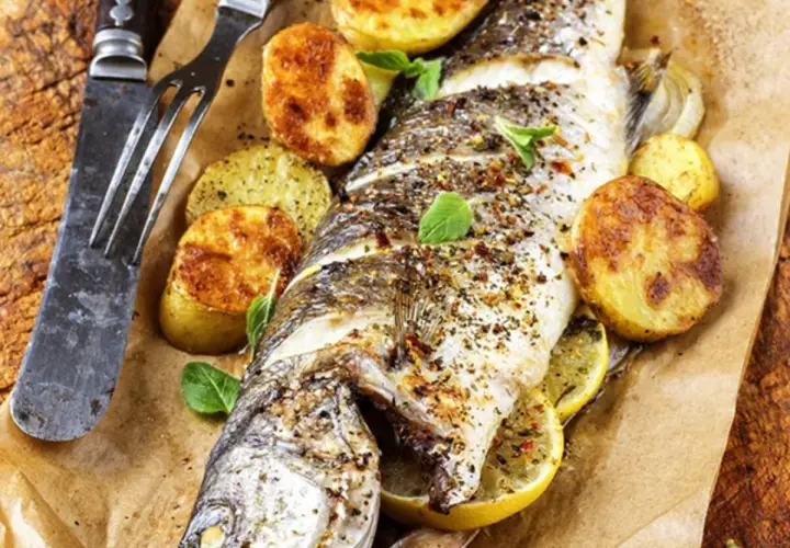 Trota salmonata al forno, dorata e saporita, servita con patate arrosto e limone. Un piatto invitante pronto da gustare.