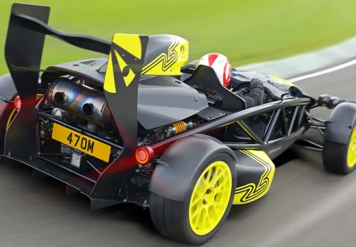 Ariel Atom na torze wyścigowym, z kierowcą w kasku, żółtymi felgami i czarnym spojlerem.