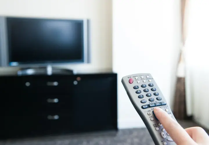Dłoń naciska przycisk na pilocie od telewizora.