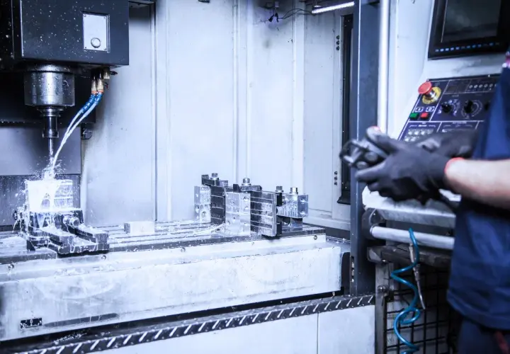 Precyzyjne wiercenie w metalu na maszynie CNC. Chłodziwo rozpryskuje się podczas obróbki. Operator w rękawicach steruje procesem.