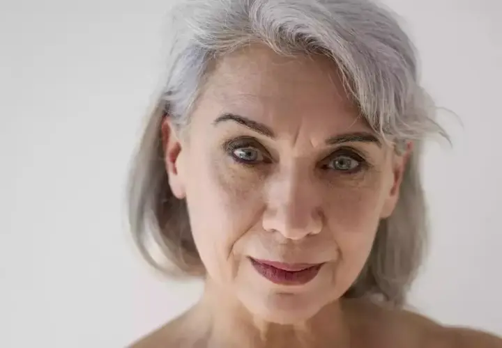 Primo piano di una donna con capelli grigi e pelle matura, che mostra i segni del tempo con grazia.